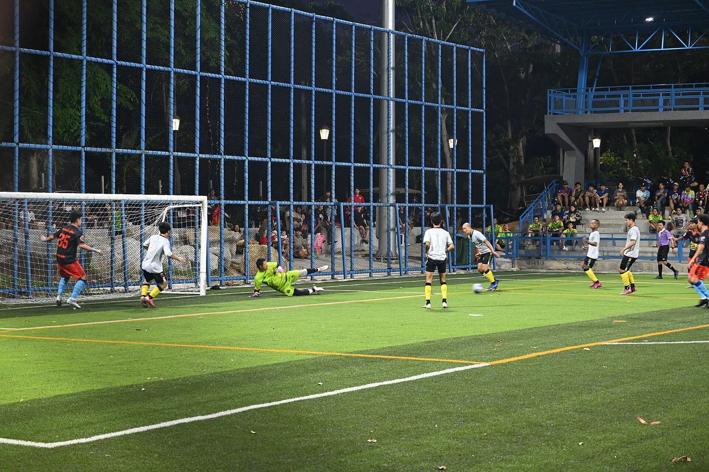 DFC 5336 A tense moment as a striker fires a shot on goal while the goalkeeper dives to make the save during a nighttime amateur soccer match.jpg